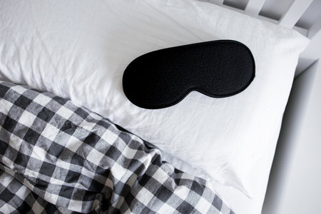 Black sleep mask on pillow and checkered blanket in bedroom settingの写真素材
