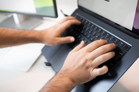 Close up of male hands typing on keyboard with laptop and monitor in background