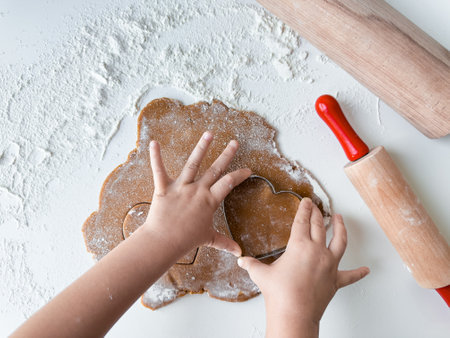 Child cutting heart shaped cookie dough with wooden rolling pins