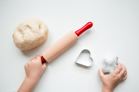 Child hands using rolling pin and cookie cutters for baking on white surfaceの写真素材
