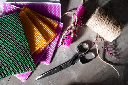 Colorful wax sheets with scissors twine and wrapped candle on a stone surfaceの写真素材