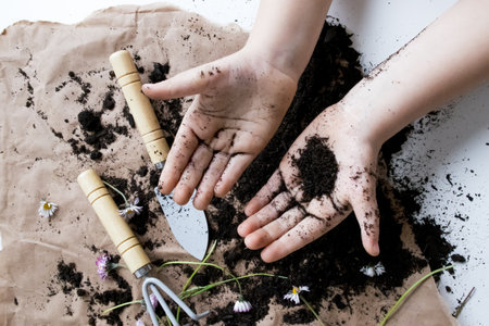 Child hands gardening with soil and flowers on brown paper