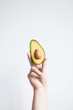 Hand holding fresh cut avocado against minimalist white backgroundの写真素材
