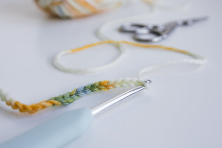 Colorful crocheting yarn with hook and scissors on white surface