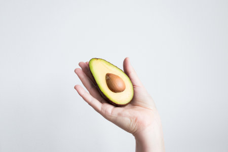 Hand holding half avocado against white backgroundの写真素材