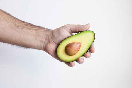 Male hand holding fresh half avocado against white backgroundの写真素材