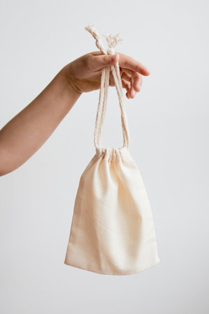 Hand holding cream cloth bag against white backgroundの写真素材