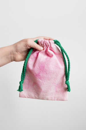 Hand holding pink drawstring bag with green rope against white backgroundの写真素材