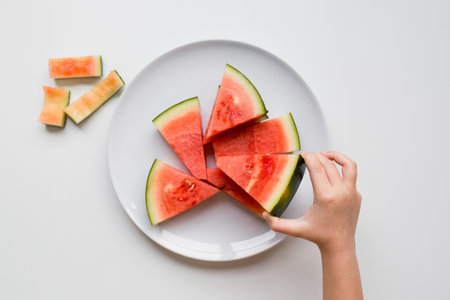 Child hand reaching for watermelon slices on a white plate