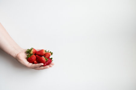 Hand holding fresh strawberries against minimalist white backgroundの写真素材