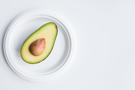Halved avocado on white plate against minimalist white backgroundの写真素材