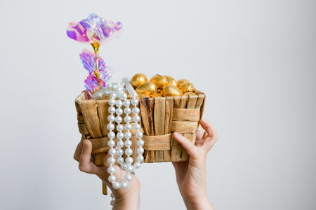 Hands holding basket of gold eggs and beaded necklace with decorative floral stick