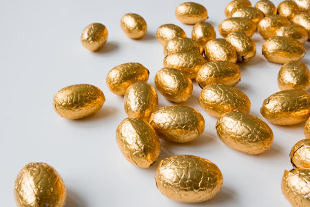 Golden foil wrapped chocolate eggs on white surfaceの写真素材