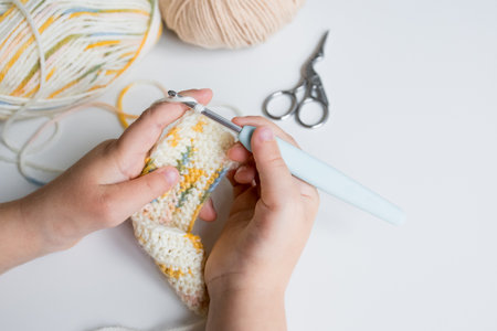 Child crocheting colorful yarn with hook and scissors on table