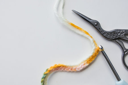 Crochet stitch pattern with colorful yarn, scissors, and hook on white background