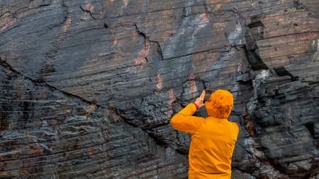 Male capturing ancient rock formations on smartphone in vibrant orange coat