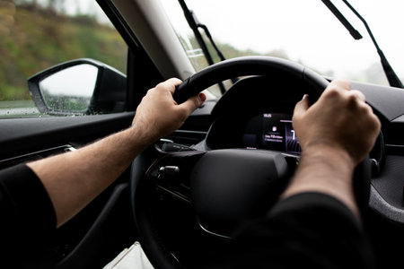 Close up of male driving a car in rainy weather with hands on steering wheelの写真素材