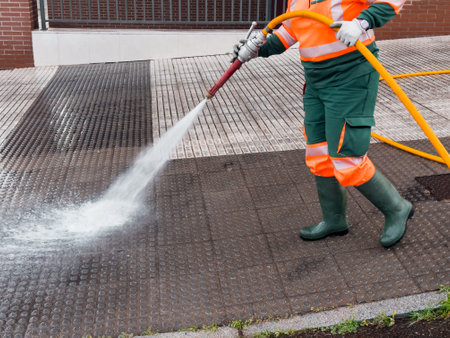 Worker power washing urban sidewalk with hose and safety gearの写真素材