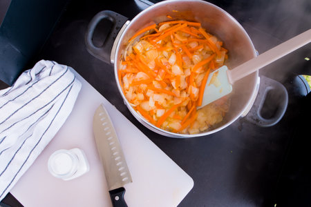 Steaming pot of sauteed onions and carrots on a black stove with knife and towelの写真素材