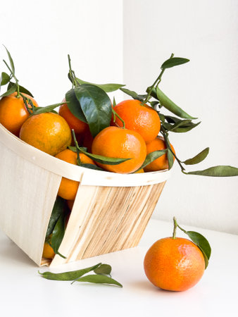 Fresh tangerines overflowing from a wooden basket on a white surfaceの写真素材