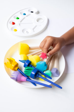 Child hand with colorful painting tools on white table