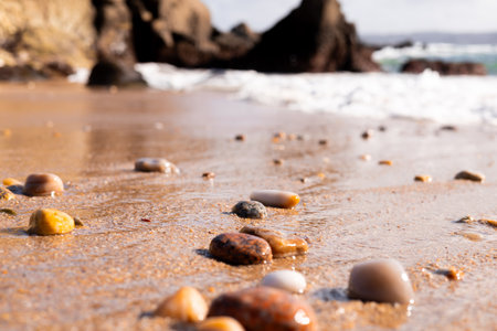 Pebble strewn beach with gentle waves and rocky backgroundの写真素材