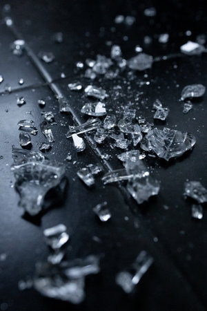 Shattered glass pieces scattered on black surface in low lightの写真素材