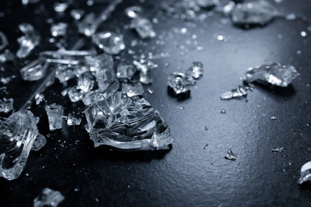 Close up of shattered glass pieces on dark surface showing textures and reflectionsの写真素材