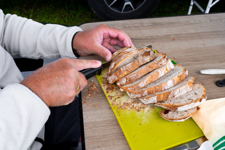Caucasian male slicing fresh bread on wooden table at outdoor picnic