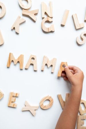 Child hand arranging wooden letters to spell MAMA on white backgroundの写真素材