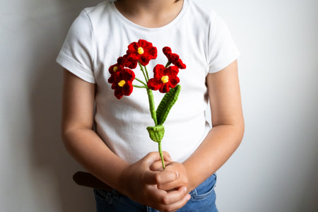 Child holding red knitted flowers in white shirt and blue jeans against white backgroundの写真素材