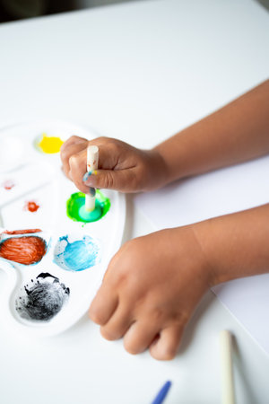 Child painting with watercolors using a brush on a white paletteの写真素材
