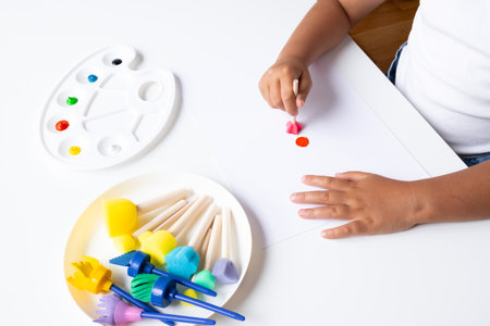 Young child painting with colorful sponges and palette on white paperの写真素材