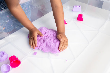 Child playing with purple kinetic sand on white tableの写真素材