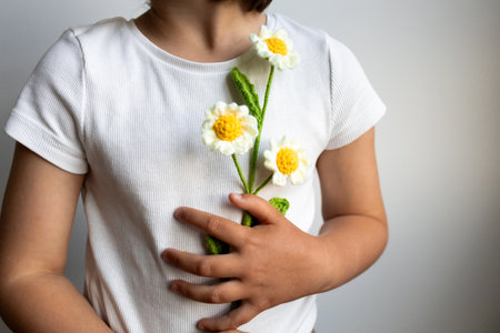 Young child holding handmade crochet flowers in white shirtの写真素材