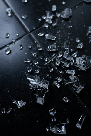 Close up of broken glass shards on dark tiled floor