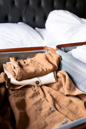 Folded clothes in open suitcase on bed with pillowsの写真素材
