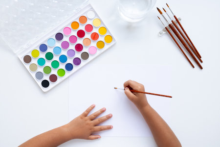 Child painting with watercolors and brushes on white paperの写真素材