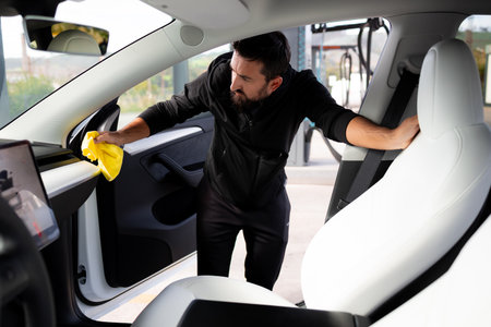 Young caucasian male cleaning car interior with yellow cloth at gas stationの写真素材