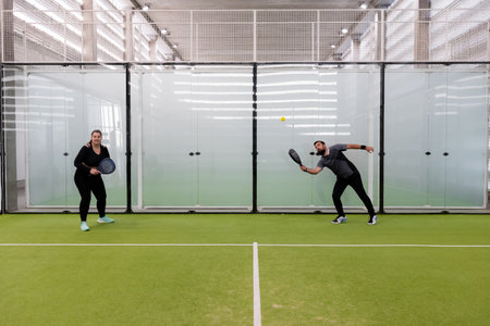 Man and woman playing indoor pickleball on green courtの写真素材