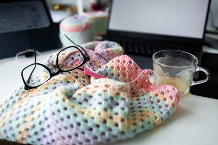Cozy knitting scene with glasses and coffee near laptop on craft table