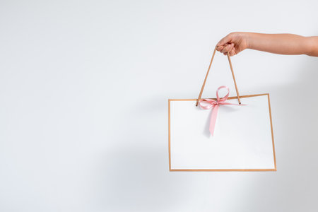 Minimalist gift bag held by caucasian female hand with pink ribbonの写真素材