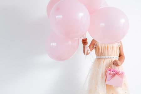 Young caucasian child in peach dress holding pink balloons and gift boxの写真素材