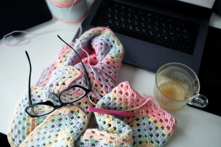 Colorful crochet project with glasses and coffee near laptop on workspace desk