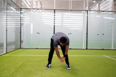 Male adult stretching on indoor tennis court with green turf