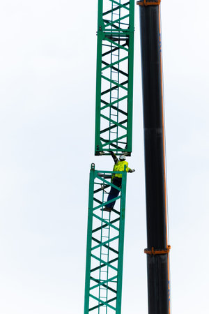 Male construction worker climbing tall crane structure in safety gear