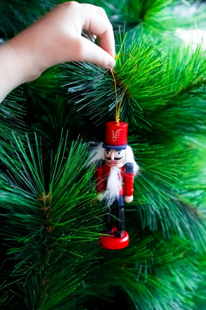 Child hand hanging nutcracker ornament on Christmas tree branchの写真素材