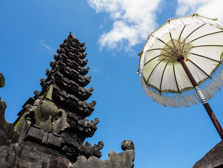 Traditional Balinese temple flanked by a white umbrella against a blue sky, Besakih temple, Bali, Indonesiaの写真素材