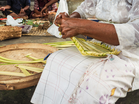 Old woman making bamboo baskets, canang sari, in a local temple in Ubud for Nyepi festivalの写真素材