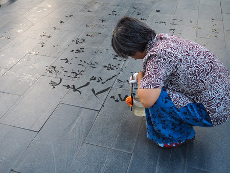 Older woman practicing water calligraphy but due to the heat the Chinese characters vanish immediately and not readable, Beijing, Chinaのeditorial素材